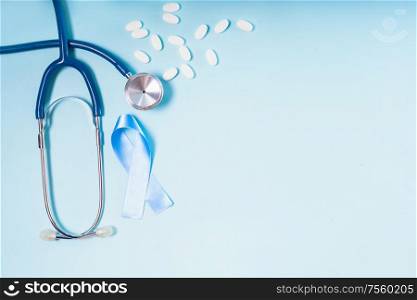 White pills, blue Diabetes Awareness Ribbon with stethoscope on blue background, copy space. White pills on blue background