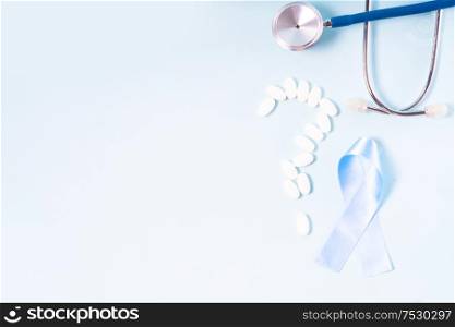 White pills, blue Diabetes Awareness Ribbon with sugar, stethoscope on blue background, copy space. White pills on blue background