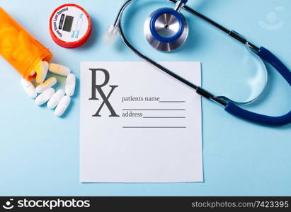 White pills in orange bottle with stethoscope on blue background, prescription and copy space on white paper note. White pills on blue background