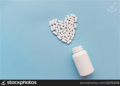 White pills in the shape of a heart and a white jar on a blue background. Pills for heart health. The concept of medicine and health care. White pills in the shape of a heart and a white jar on a blue background. Pills for heart health. The concept of medicine and health care.