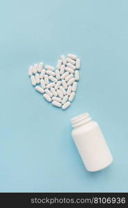 White pills in the shape of a heart came out of a jar on a blue background, health and heart problems together with a plastic jar. The concept of medicine and health care. Place for writing. White pills in the shape of a heart came out of a jar on a blue background, health and heart problems together with a plastic jar. The concept of medicine and health care. Place for writing.