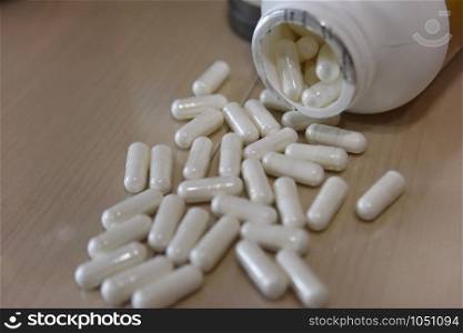 white pills in thewhite plastic bottle on the wooden table