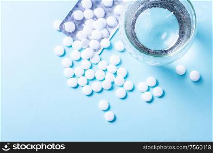 White pills with glass of clear water over blue background with copy space. Pile of pills