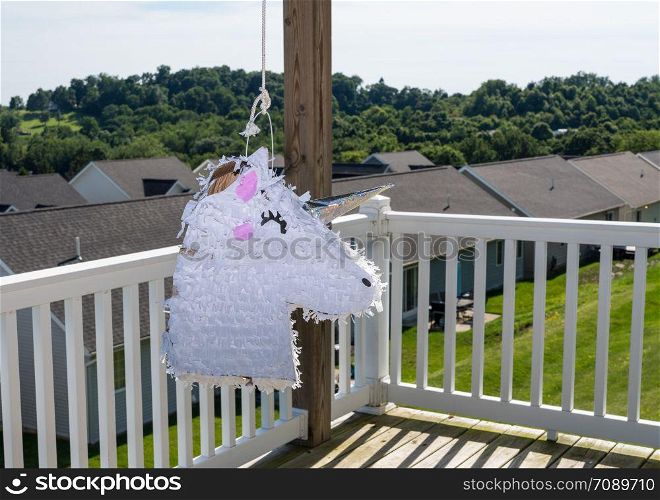 White pinata shaped like a unicorn hanging on the deck of modern home in USA for childs party. White unicorn shaped pinata after being beaten at childs party