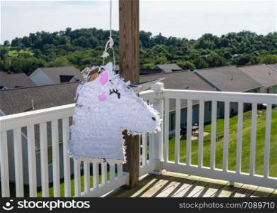White pinata shaped like a unicorn hanging on the deck of modern home in USA for childs party. White unicorn shaped pinata after being beaten at childs party