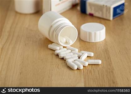 White plastic bottle for medicines. Scattered white pills and drug boxes in the background.. White plastic bottle for medicines. Scattered pills and drug boxes in the background.