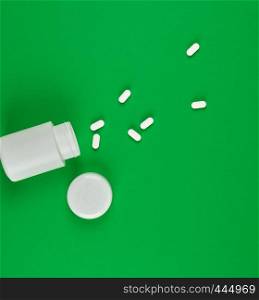 white plastic can and scattered oval pills on a green background, top view