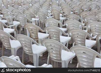 White plastic chairs in row stand ready for visitors of a concert or performance show. White plastic chairs in row stand waiting for visitors