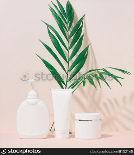 White plastic container tube, a jar with a lid and a container with a dispenser for cosmetics on a beige background with a shadow from a palm leaf. Advertising and promotion