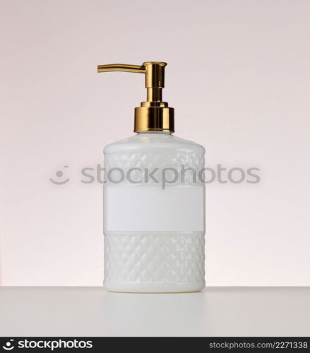 white plastic container with a golden dispenser on a beige background. Container for liquid soap, sh&oo