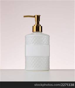 white plastic container with a golden dispenser on a beige background. Container for liquid soap, sh&oo