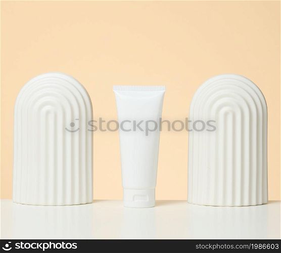 white plastic tube for cosmetic liquid products on a white table. Promotion and advertising of products, beige background