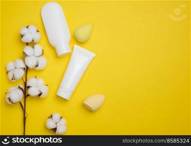 White plastic tubes  and jar for cream, gel and other cosmetics and sponges on a yellow background, top view
