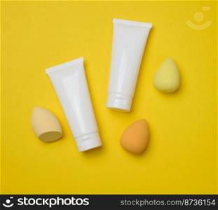 White plastic tubes for cream, gel and other cosmetics and sponges on a yellow background, top view