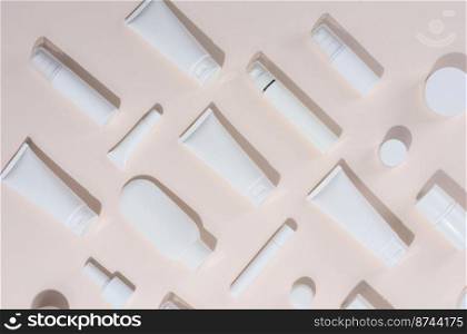 White plastic tubes, jars and other form of packaging for cosmetics on a beige background, top view. Template for branding, advertising and product promotion