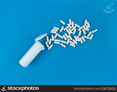 White plastik medical bottle and scattered pills capsules on a blue backdrop with copy space.. White plastik medical bottle and scattered pills capsules on blue backdrop with copy space.
