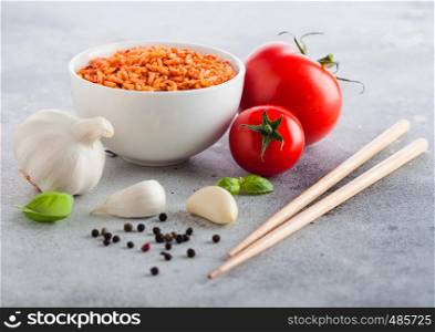White plate bowl of rice with tomato and basil and garlic and chopsticks on light stone background. Traditional food