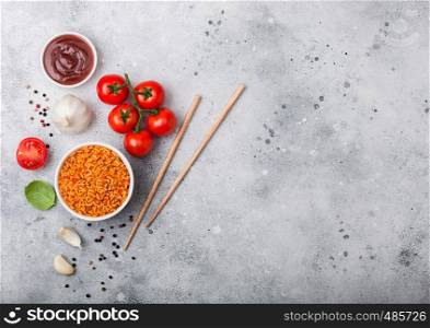 White plate bowl of rice with tomato and basil and garlic and chopsticks on light stone background. Top view.