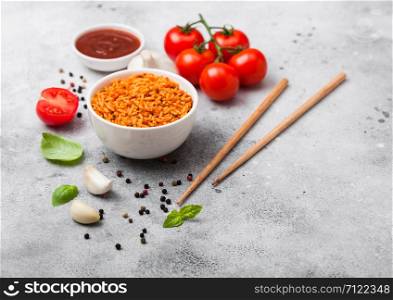 White plate bowl of rice with tomato and basil and garlic and chopsticks on light stone background. Traditional food
