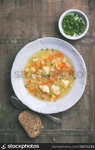 White plate of homemade vegetable soup on wooden background, top view