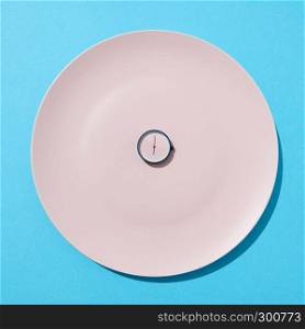 White plate with whatch shows six o'clock on a blue background, copy space. Flat lay. Concept of limiting the intake of food diet and weight loss.. Round watch six o'clock on white plate on a blue background. Time to eat and diet concept. Place for text. Top view.