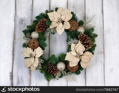 White Poinsettia flower and pine cone Christmas wreath on rustic white wood.