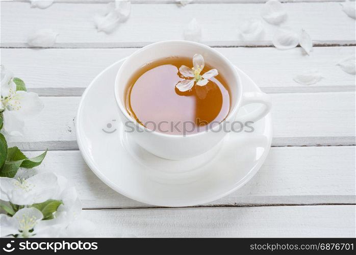 White porcelain cup cup of green tea and apple-tree flowers on an old white wooden shabby background