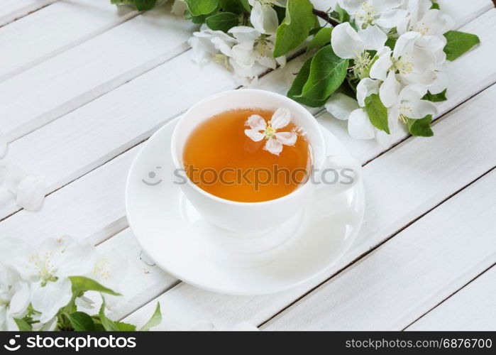 White porcelain cup cup of green tea and branches of apple-tree flowers on an old white wooden shabby background