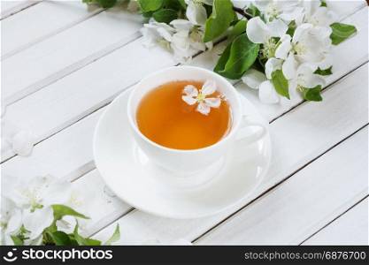 White porcelain cup cup of green tea and branches of apple-tree flowers on an old white wooden shabby background