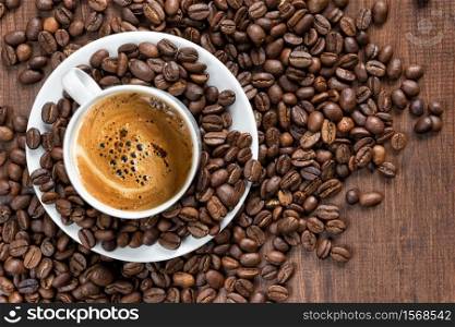 White porcelain cup of coffee and roasted coffee beans are on the wooden background, top view