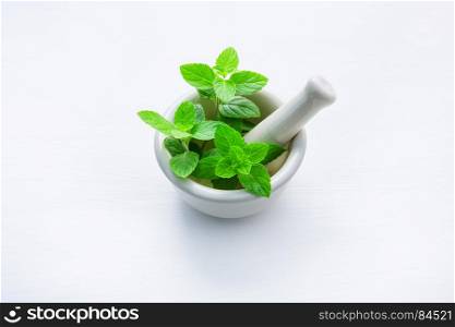 White porcelain mortar and pestle with peppermint leaf on white wooden background with copy space.