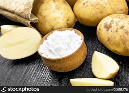 White potato starch in bowl, vegetable tubers in a bag and on a table against the background of wooden board