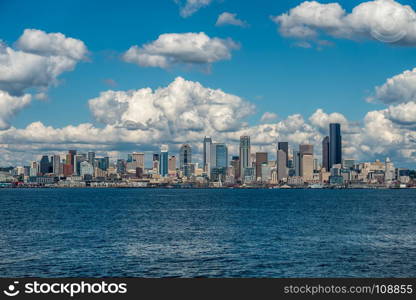 White puffy clouds hover over the Seattle skyline on a sunny day.