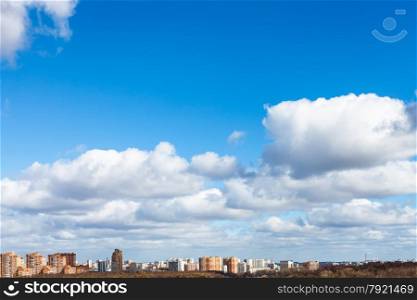 white puffy clouds in blue spring sky over city