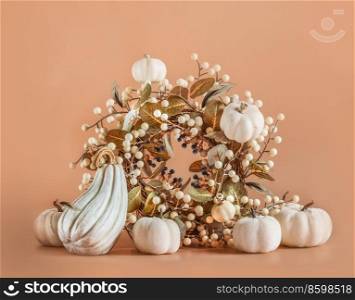 White pumpkins arrangement with seasonal branch and autumn leaves at orange background. Beautiful fall decoration with wreath. Front view.