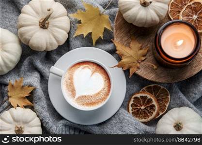 White pumpkins, coffee and autumn leaves on a grey knitted sweater. Autumn home decor.