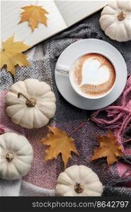 White pumpkins, coffee and autumn leaves on a plaid. Autumn home decor.