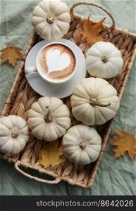 White pumpkins, coffee and autumn leaves on a wicker tray. Autumn home decor.