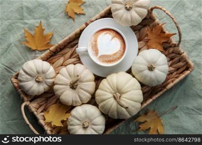White pumpkins, coffee and autumn leaves on a wicker tray. Autumn home decor.
