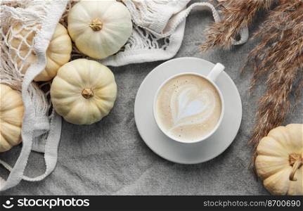 White pumpkins, coffee and pampas grass on a grey textile background. Autumn home decor.