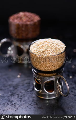 White raw quinoa in a glass cup, red quinoa on back, dark background, selective focus