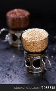 White raw quinoa in a glass cup, red quinoa on back, dark background, selective focus