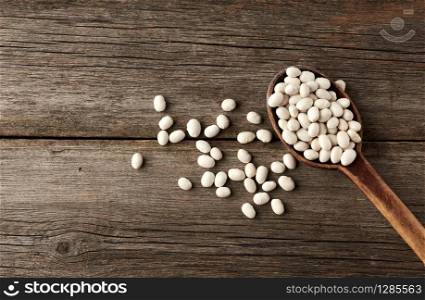 white raw whole beans in a brown wooden spoon on the table, top view