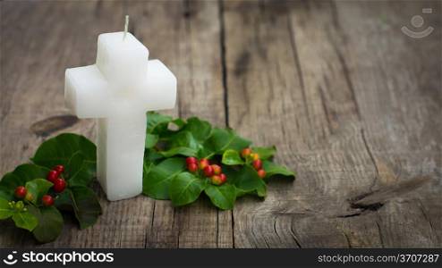White Religious Candle surrounded by green leaves on wood background
