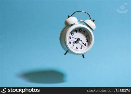 White retro style alarm clock flying on blue background throwing hard shadow. Flying analog clock.
