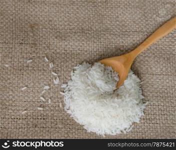 white rice grains on sackcloth. white rice grains with wooden spoon on sackcloth