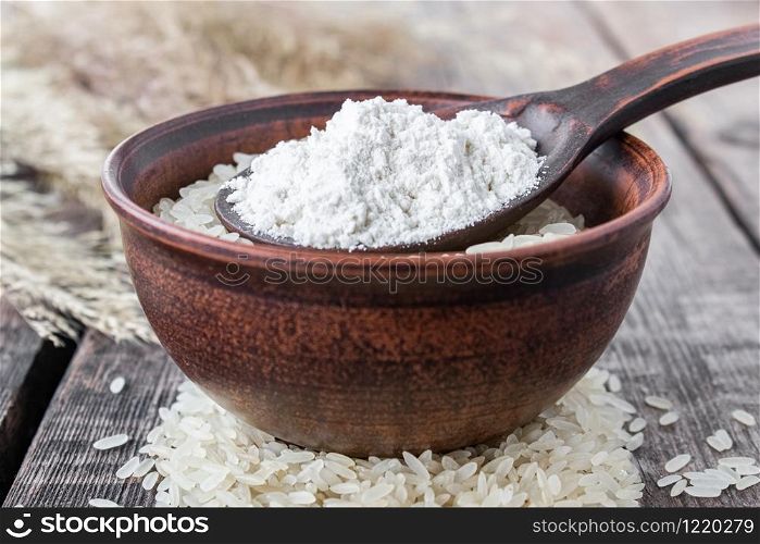White rice in a bowl with a spoon of white flour on a background of old boards. Jasmine rice for cooking. Close-up.. White rice in a bowl with a spoon of white flour on a background of old boards. Jasmine rice for cooking.
