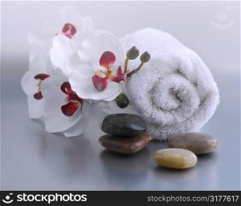 White rolled up towel with massage stones and an orchid