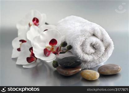 White rolled up towel with massage stones and an orchid