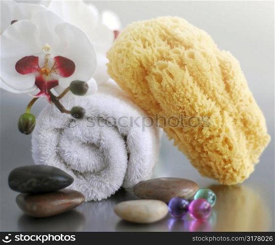 White rolled up towel with massage stones, orchid and natural sponge
